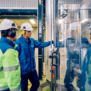 Deux techniciens en casque et protections auditives inspectent une pompe à chaleur industrielle