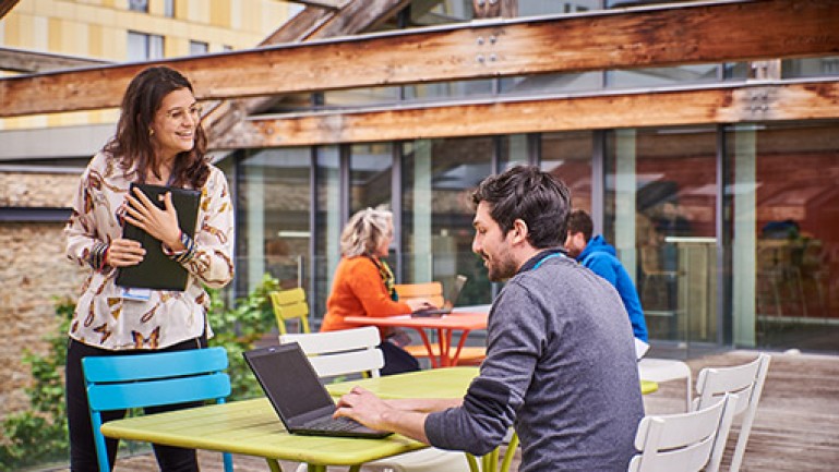 Homme travaillant sur son ordinateur en extérieur et échangeant avec une collègue